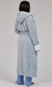 A model shown from the back wearing a light blue textured hooded robe with white cuffs and a matching belt, paired with blue pajama pants, against a neutral gray studio background.