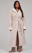 A woman modeling a long cream-colored textured robe with white faux-fur trim, worn over brown lounge pants against a neutral light gray studio background.