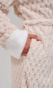 Close-up of a textured cream-colored plush robe with a white sherpa-lined cuff and a hand tucked into a front pocket.