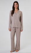 A woman modeling a two-piece pajama set in a light taupe-beige color, featuring a long-sleeve button-front top with a collar and matching wide-leg pants, shot against a plain light gray studio background.