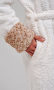 A woman wearing a plush white bathrobe with a leopard patterned hood and cuffs, posed against a neutral light gray background.