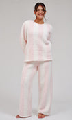 A woman modeling a two-piece fuzzy fleece pajama set with light pink and white vertical stripes, consisting of a long-sleeve top and matching wide-leg pants, against a light gray studio background.