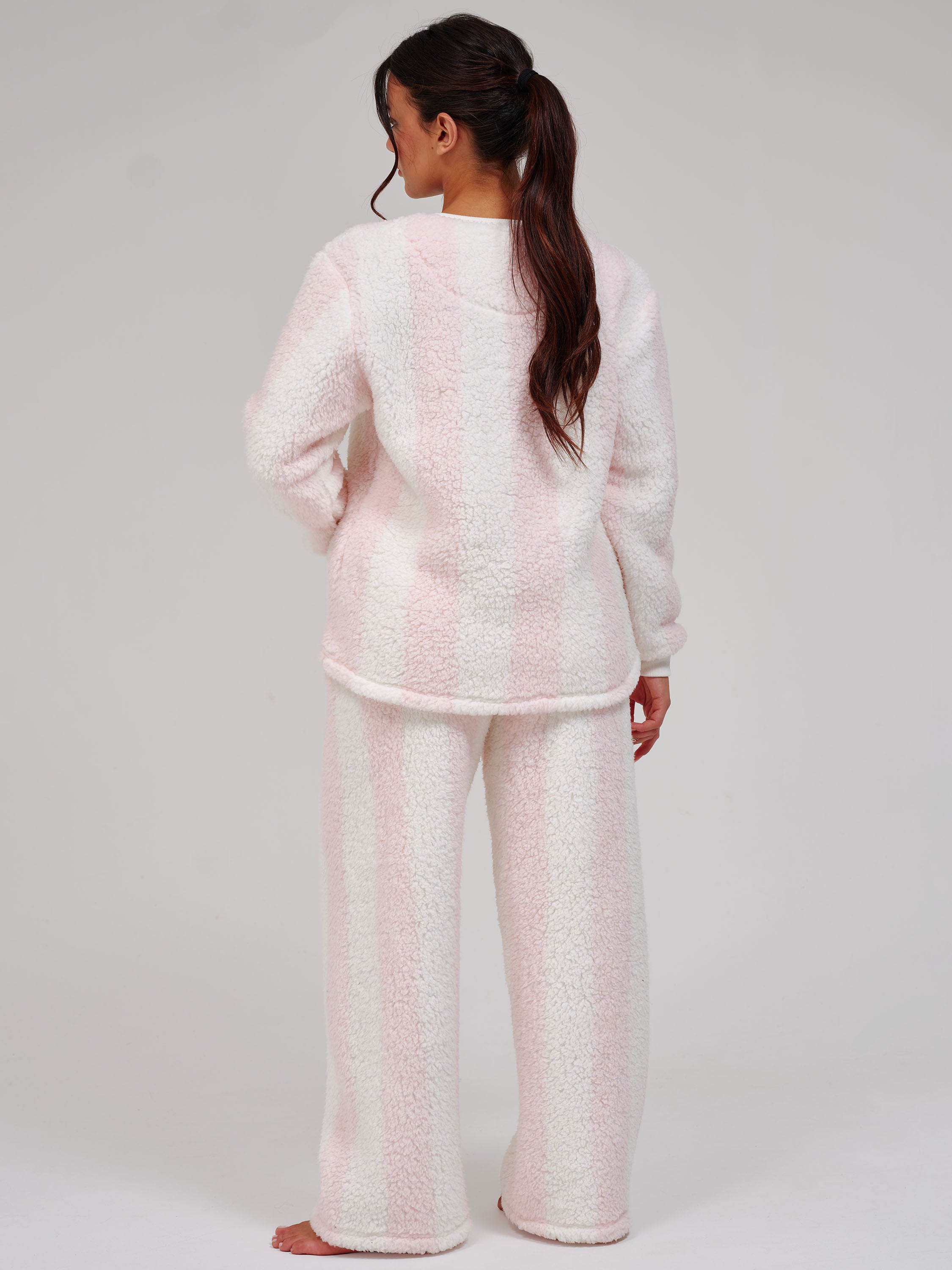 A woman wearing a light pink fuzzy fleece pajama set, shown from the back against a plain light gray studio background.