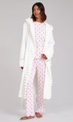 A woman modelling a two-piece pajama set with a long white faux-fur robe. The pajama set consists of a light pink long-sleeve top and matching pants, both patterned with small pink cowboy boot motifs.